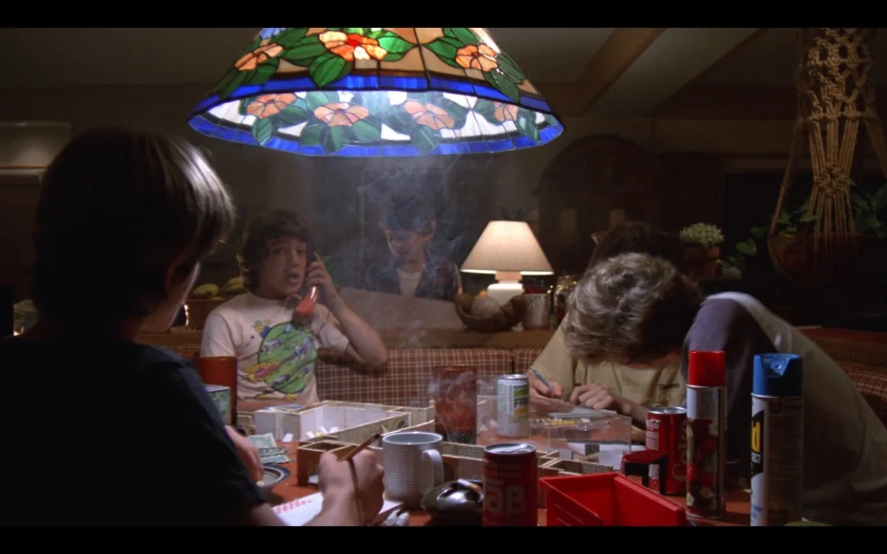 Scene from E.T. at the kitchen table where the kids are playing D&#x26;D, smoking cigarettes, drinking soda, and the table is a mess. A can of Raid can be seen at one end of the table.